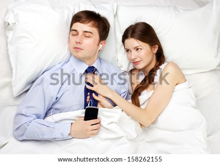 young businessman in shirt and necktie with phone and young beautiful attract girl in a bed on white background
