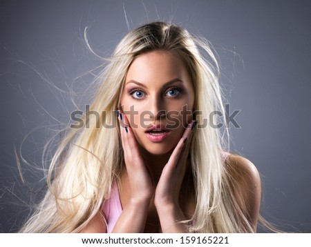 portrait of amazed  blond young woman with waving hair and opened mouth on grey background