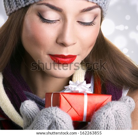 closeup portrait of a beautiful young woman in hat and gloves with gift  box on grey bokeh background