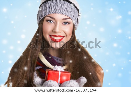 beautiful young woman in hat and gloves with present's box on snow and blue background