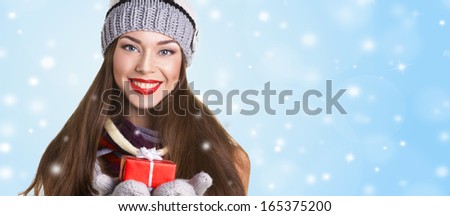 beautiful young woman in hat and gloves with present\'s box on snow and blue background