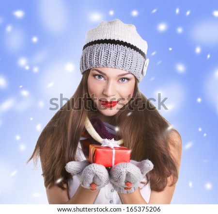 young woman in hat and gloves with  gift red box on snow and blue sky background