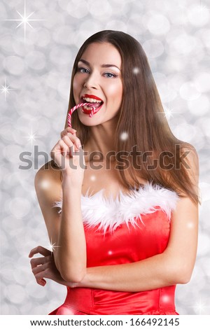 beautiful sexy girl in red christmas dress eating candycane on bokeh and star grey background