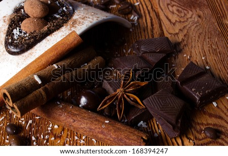tasty still - heap of  coconut flakes, chocolate, sticks of cinnamon and anise, and white modern plate with brown ball candy on wooden table