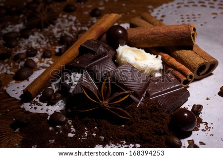 heap of  candy with coconut flakes, chocolate ball, ground coffee, coffee beans and sticks of cinnamon and anise on white napkin on wooden table