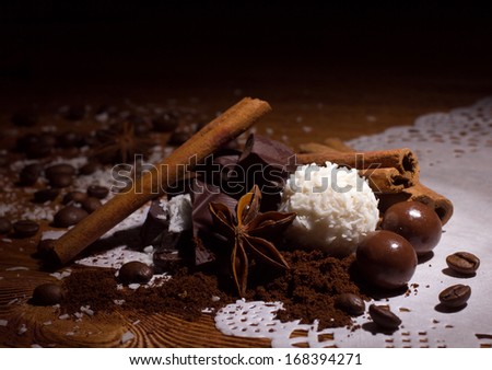 pile of  candy with coconut flakes, chocolate ball , ground coffee, coffee beans, sticks of cinnamon and anise on white napkin on wooden table