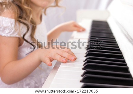 little girl with  long curls in white fashion dress playing on white piano, close-up