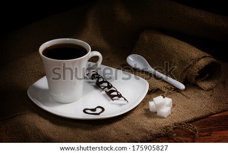 coffee in white cup on white plate, near - ceramic spoon and sugar lumps on sacking, on plate drawn hearts and chocolate