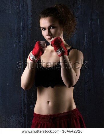 portrait of a sexy young woman boxer in red and black clothes  ready to fight  on dark grey background