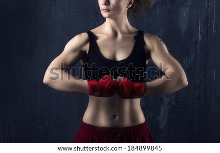 Portrait of a young brunette woman body-builder with beautiful musculature on dark grunge background