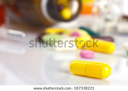 drug in yellow capsule on white table and blurred background with different medicament in blisters and bottle