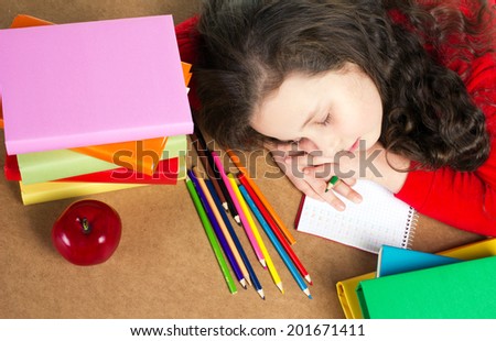 tired school little girl sitting  at the table with school accessories and red apple and sleep, top view