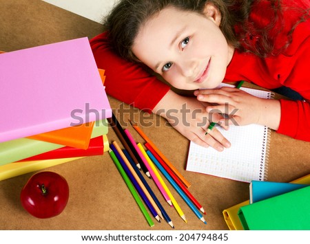 smiling beauty little girl with copybook, red apple, many colorful books and pencils, top view