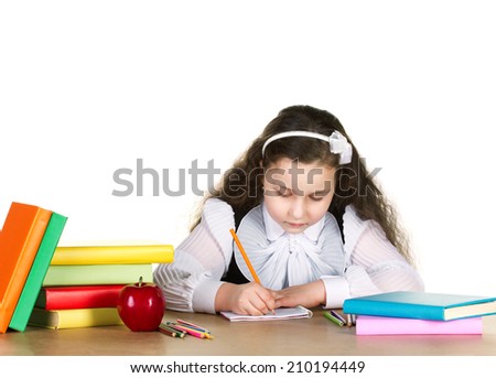 beauty little girl  in white and black uniform diligently writing in copybook, near -  red apple, many colorful books and pencils