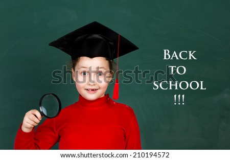 little funny girl holding magnifying glass and  trying university hat on chalkboard background