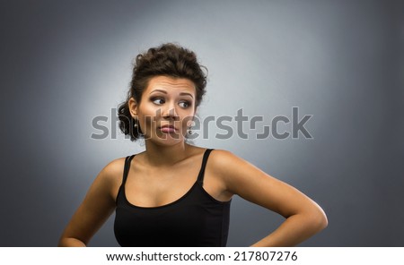 portrait of young emotion woman with curl brown hear in black tank top on light grey background