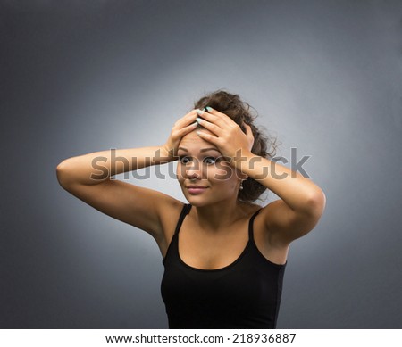 surprised young brunette woman holding her head, isolated on grey light background