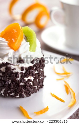 cake with cream, chocolate crumb, slices of tropical fruits and orange skin  on white plate, macro shot