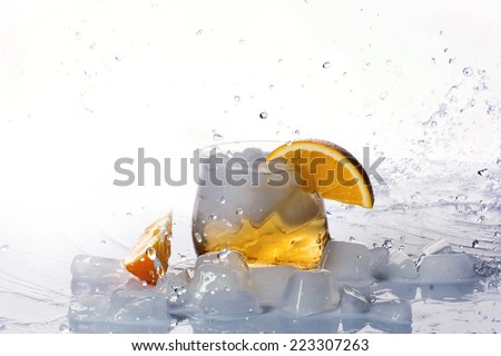 Orange drink, ice-cubes and orange slice in glass,  ice-cubes,  orange slice and water splashes on transparent surface, white background with place  for your text