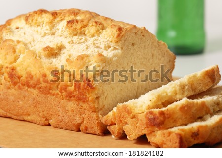 A loaf of freshly baked beer bread on a cutting board with three slices cut and a beer bottle out of focus in the background