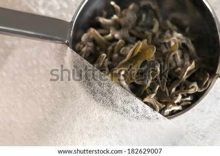A close-up of natural organic dried tea leaves being spooned into a natural fiber tea bag to eliminate potentially hazardous chemicals that go into the processing of tea and bleaching of the tea bags