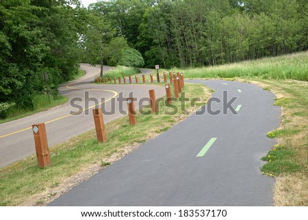 Long, curvy and sloped road in a park-like area, with lanes for autos and lanes for pedestrians and bicyclists separated by a wooden fence