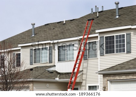 An extension ladder leans against the front of a multifamily housing building in preparation of roof repairs
