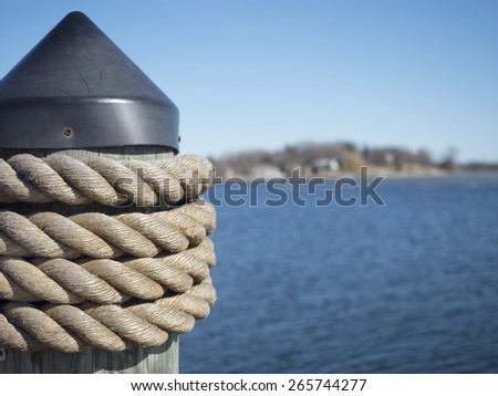 Post with rope at the side of a pier for docking and securing boats.  Selective focus on the rope.  Background of shoreline and water are obvious but deliberately blurred.