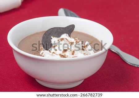 A dish of chocolate pudding / custard, topped with a dollop of whipped cream and garnished with powdered cocoa powder and a chocolate wafer.