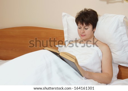 Woman reads a book lying in her bed