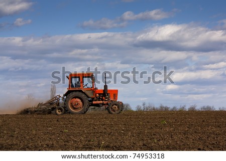 Old red tractor tilling a field with a cloudy spring sky