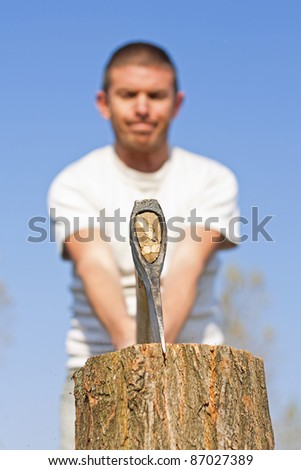 Close up of axe head splitting a log with a male figure with narrow depth of focus against a beautiful blue sky