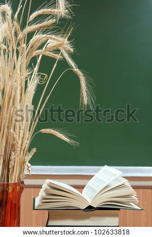 exposed book lies on the pile of books next to a red vase and ears of wheat on a background a green school board