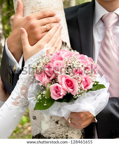 hands of the groom and the bride on a background of birch trees with a bouquet of flowers