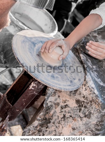 hand of the girl on a potter\'s wheel helps potter with clay