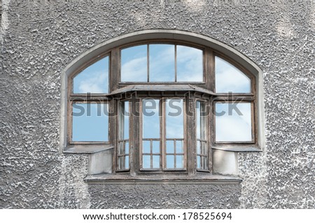 old window at the gray wall with the reflection of the sky on glass