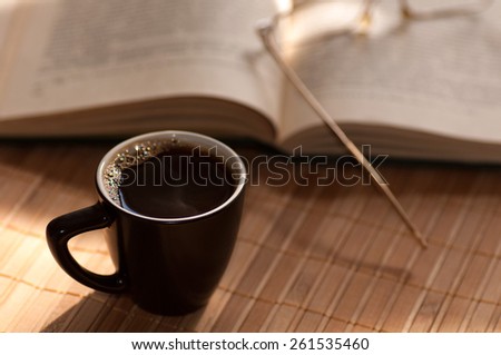 cup of coffee, standing next to an open book, on which lie glasses