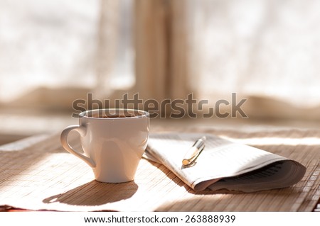 Cup of black coffee, newspaper and a pen against the window in the morning