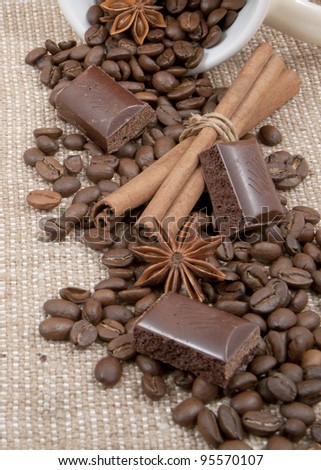 bob of coffee, chocolate, sticks of cinnamon, anise spilled from a cup on a background rough material