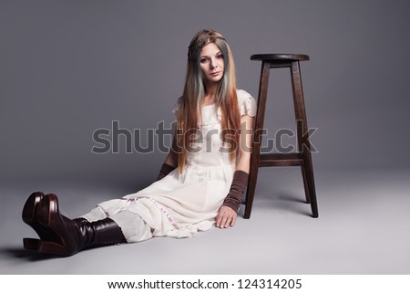 hippie like young lady sitting down on the floor with a stool next to her