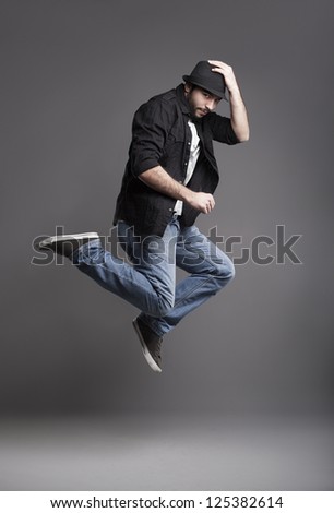 young male model jumping,holding his hat and looking at camera on grey background
