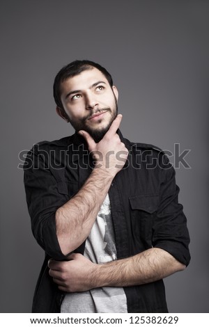 young man standing and thinking while his hand on his chin