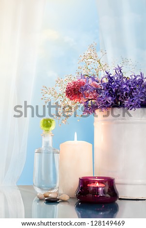 still life with various flowers and a bottle of liquid in front of an open window