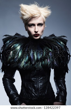 fashion model wearing a costume made of leather and feathers posing on blue background
