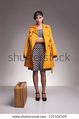 young fashion model wearing yellow topcoat standing and posing with her leather retro suitcase