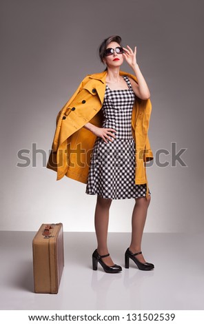 beautiful young woman with yellow coat and sunglasses posing on grey background