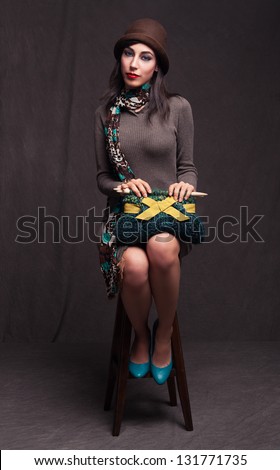 young beautiful lady sitting on a stool and holding a knitted hand bag on grunge background