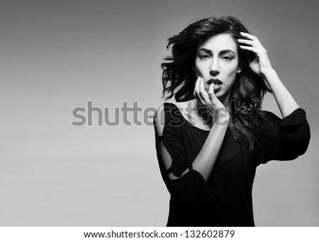 black and white picture of beautiful tempting brunette bites her finger on grey background with copyspace