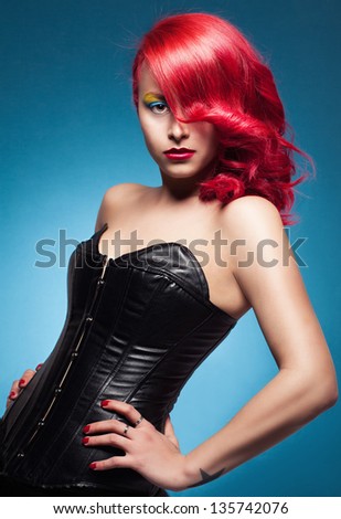 young lady with colorful hair and make up, wearing a black strapless and posing on blue background
