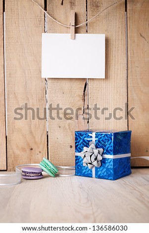 gift box and macaroons on a wooden table in front of a wooden wall with blank paper hanged